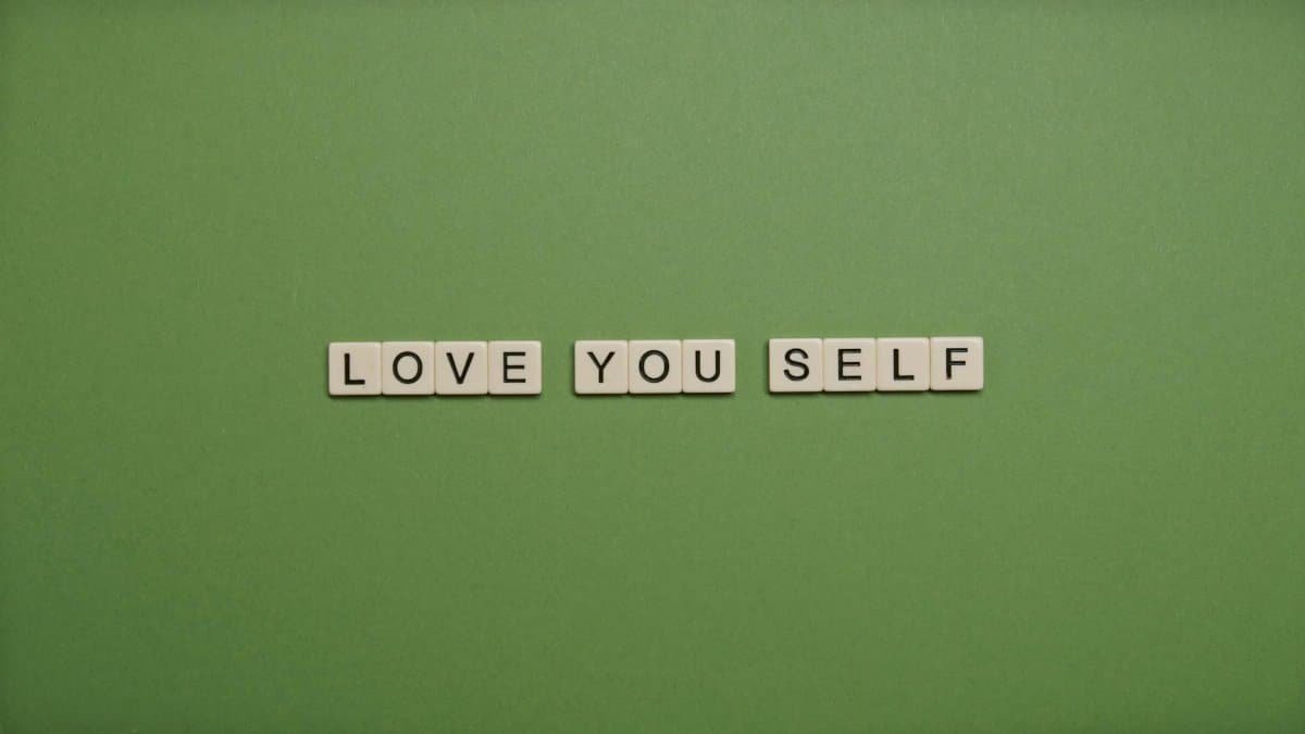 Positive message 'Love You Self' spelled with letter tiles on green background.