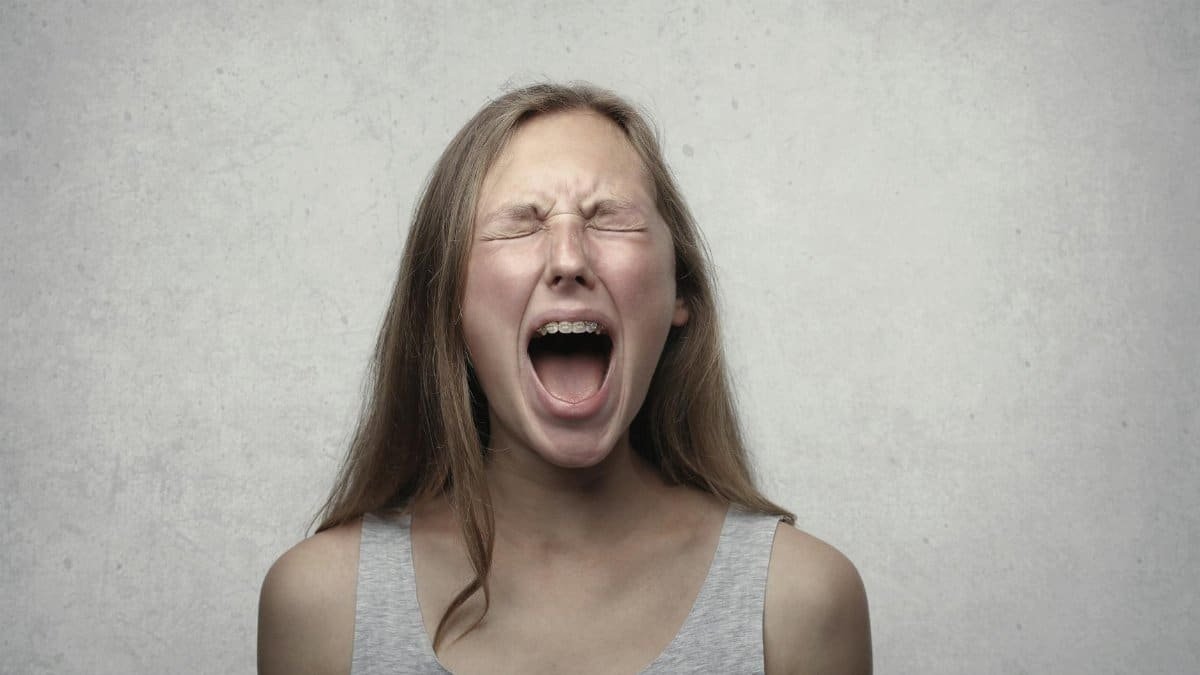Young woman screaming with emotion, showing braces, against a gray backdrop.
