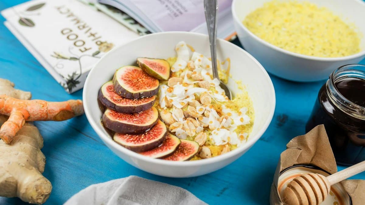 Healthy breakfast bowl with figs, nuts, and turmeric on a blue table with ginger and honey.