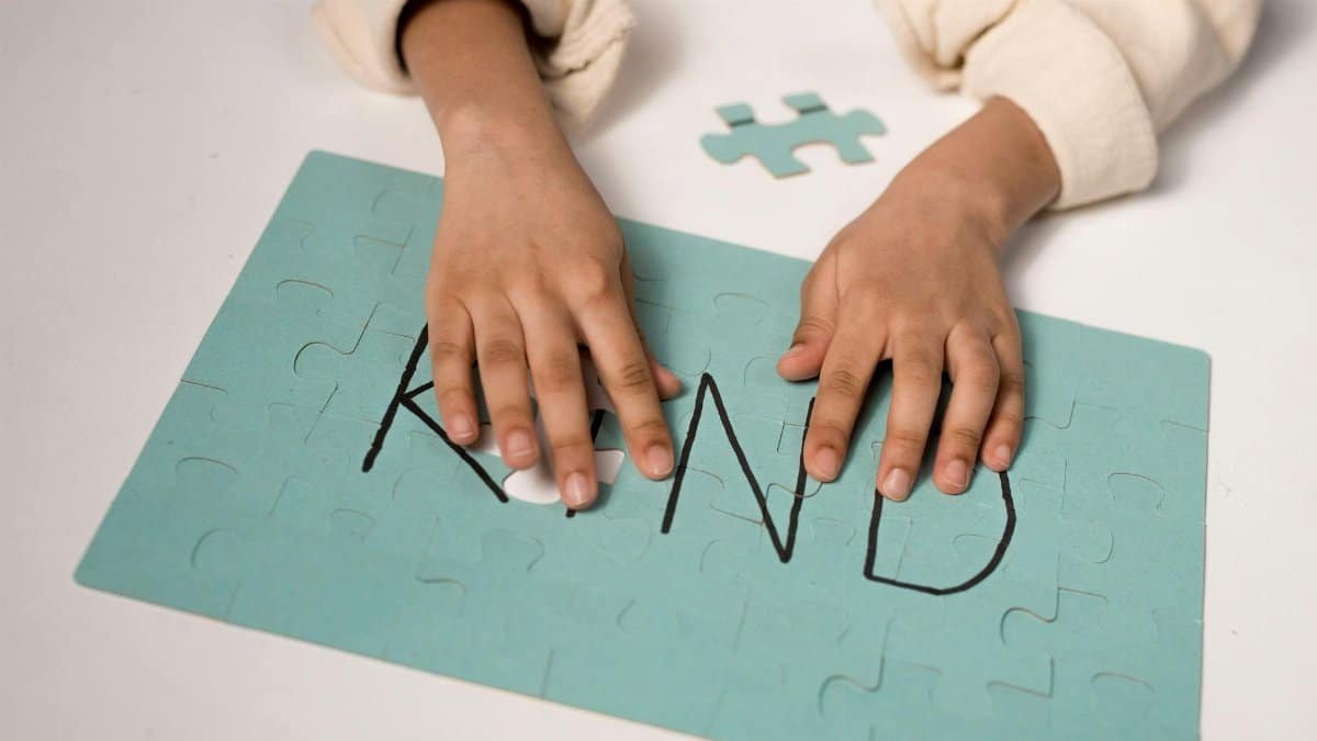 Close-up of child assembling puzzle spelling 'Kind' emphasizing kindness.