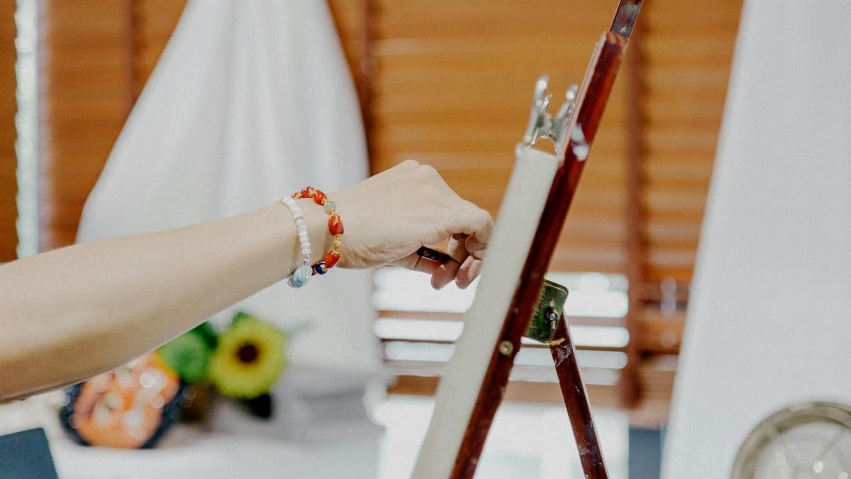 Close-up of an artist painting on canvas with an easel and vibrant bracelet in a studio setting.