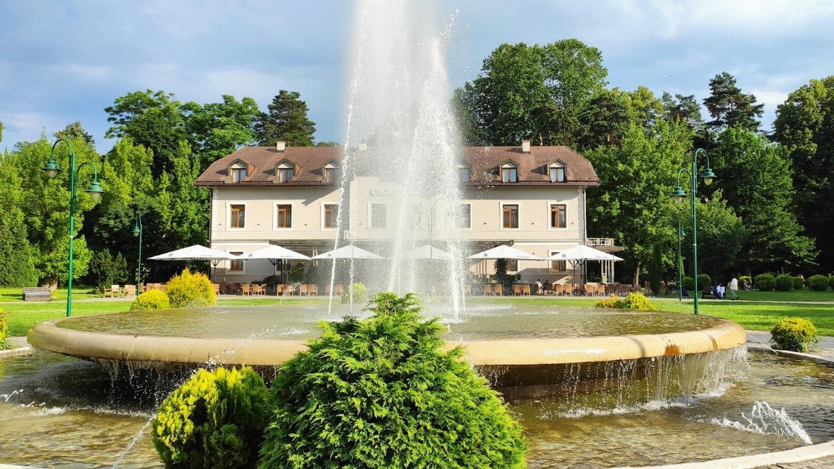 Scenic view of a fountain and building in Ilidža Park, showcasing lush greenery and a serene atmosphere.