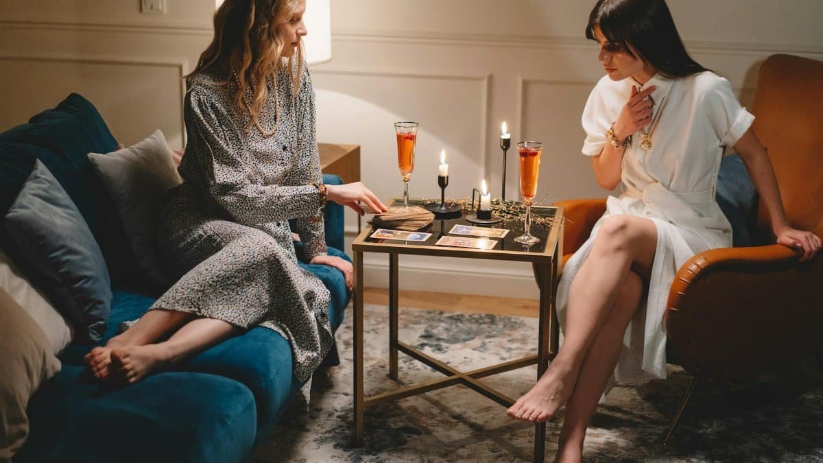 Two women enjoying a tarot reading session with candles and wine in a cozy indoor setting.