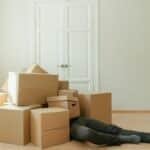 Person on floor surrounded by cardboard boxes during moving; concept of stress and relocation.