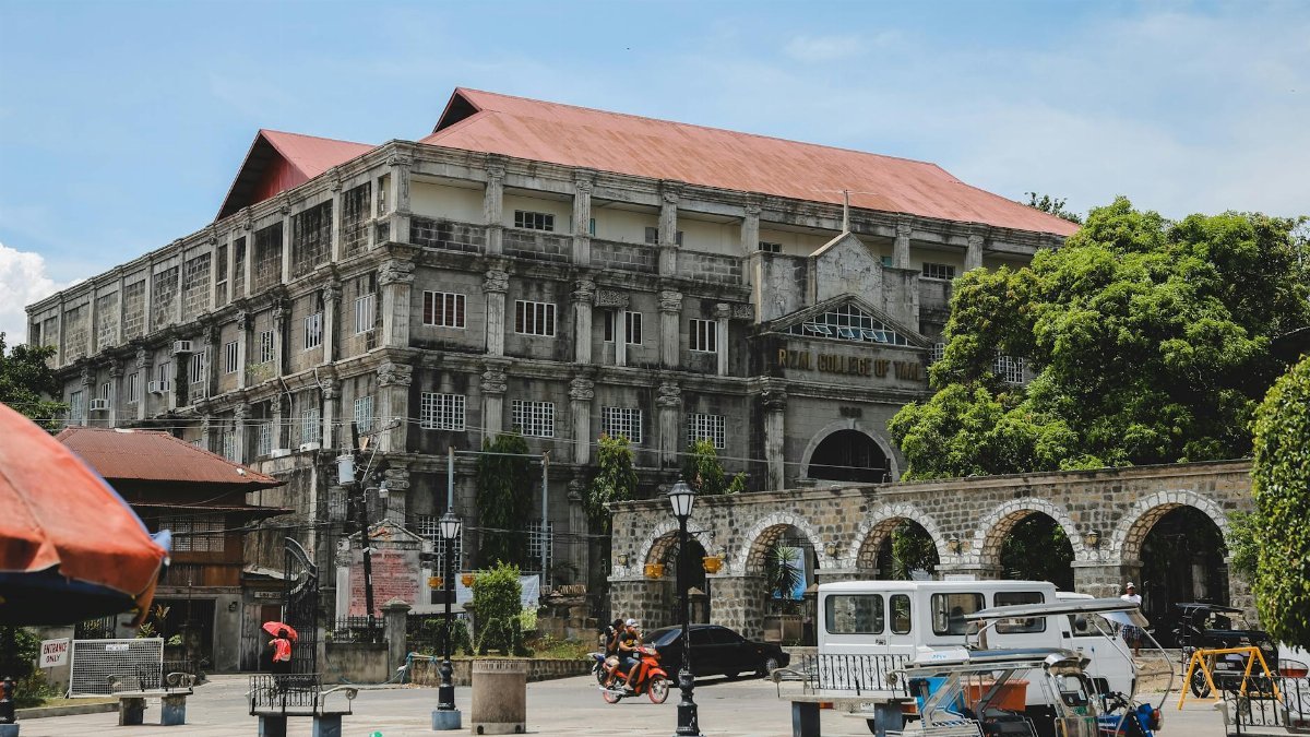 A classic college building surrounded by vibrant urban life and trees.