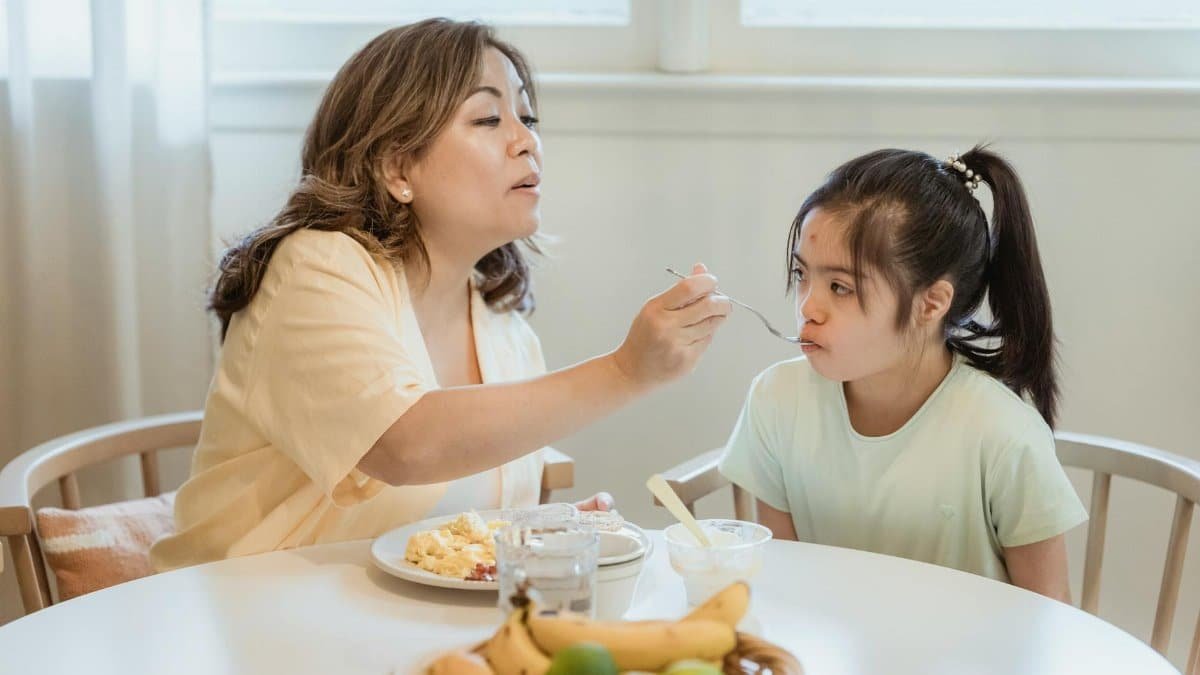 A mother lovingly feeds her daughter breakfast in a cozy home setting.
