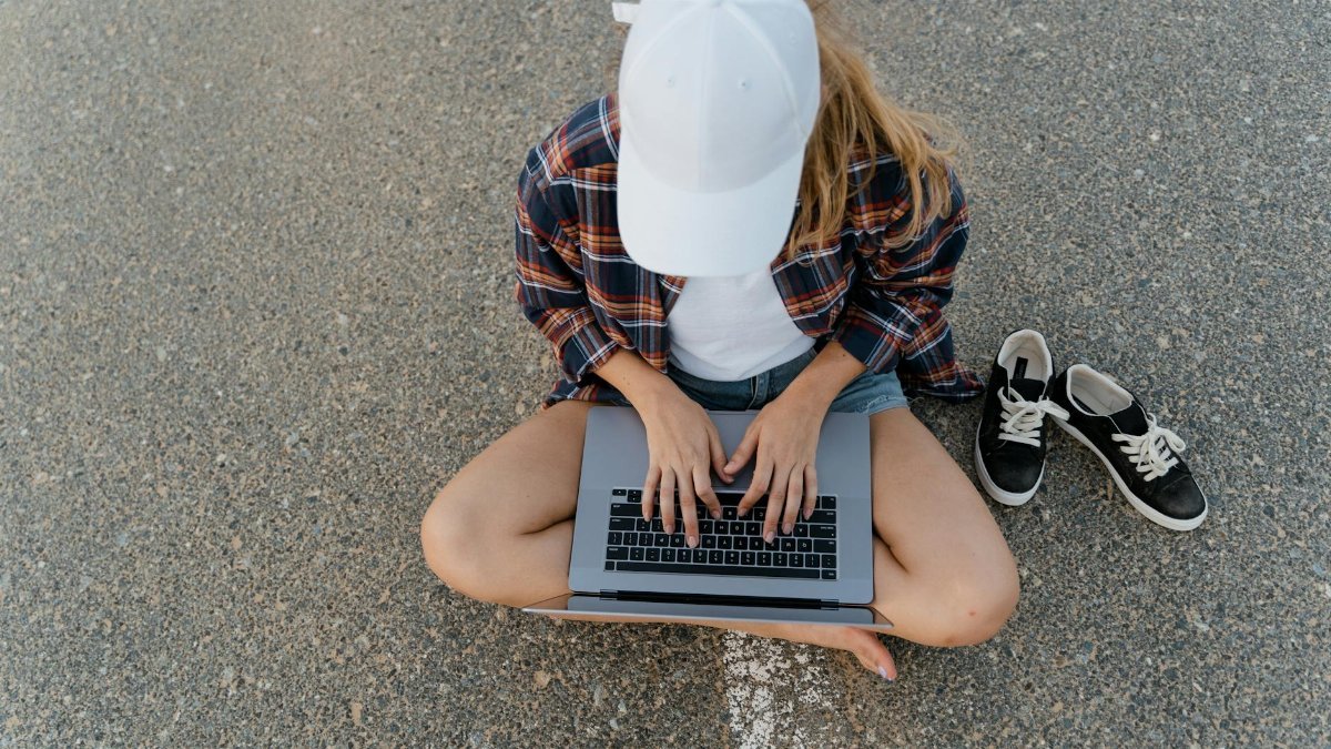 High-angle view of a woman working on a laptop while sitting on asphalt, embodying the digital nomad lifestyle.