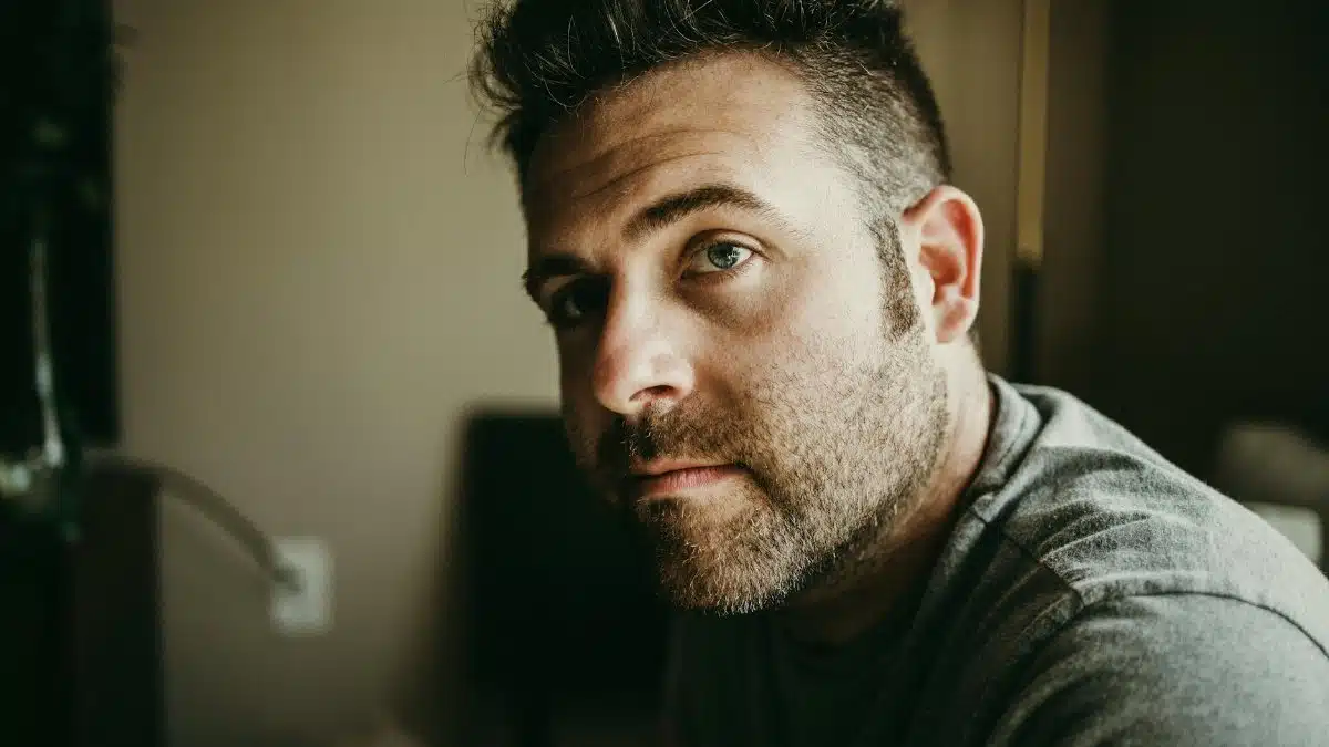 Close-up portrait of a thoughtful bearded man indoors with moody lighting.