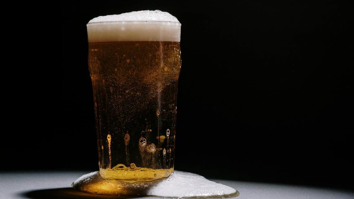 A studio shot of a frothy and overflowing pint of golden beer against a dark backdrop.