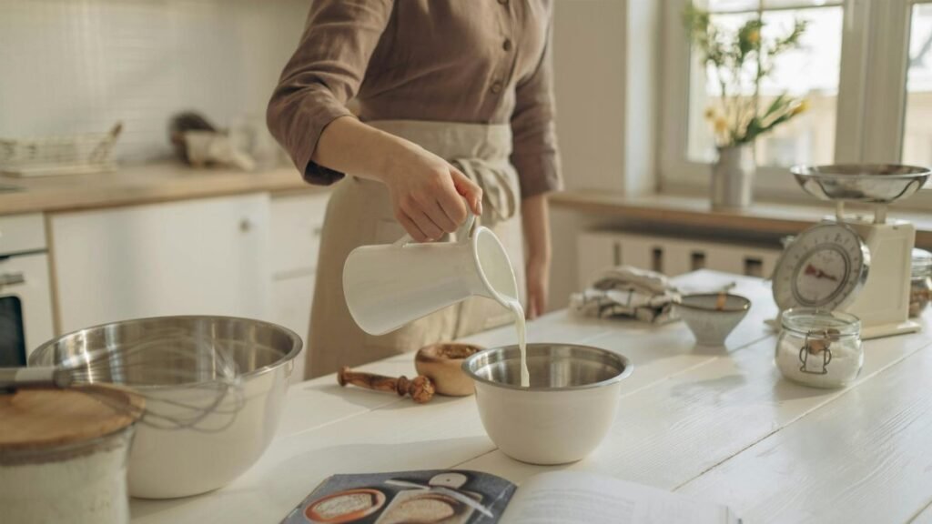 A person pours milk into a bowl, preparing ingredients on a kitchen island for baking.