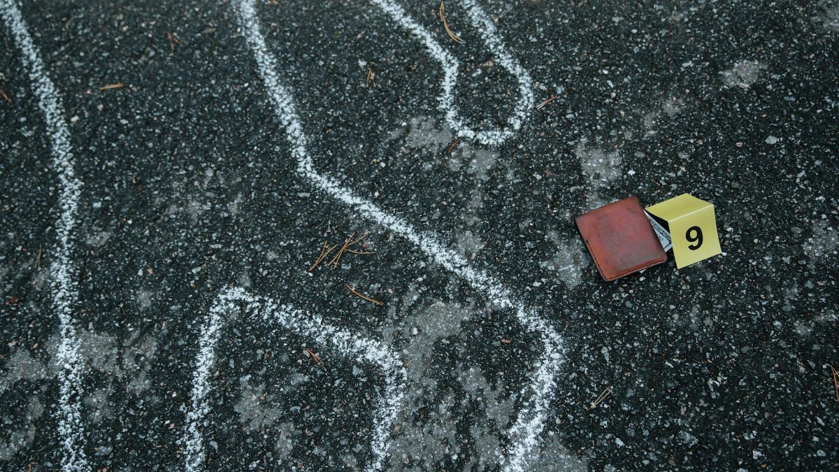 Crime scene with a chalk outline and evidence marker on asphalt.
