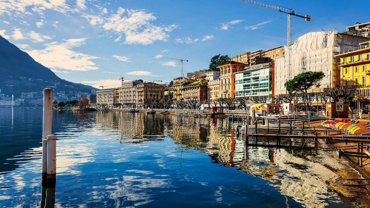A picturesque lakeside cityscape with colorful buildings and clear reflections on a sunny day.