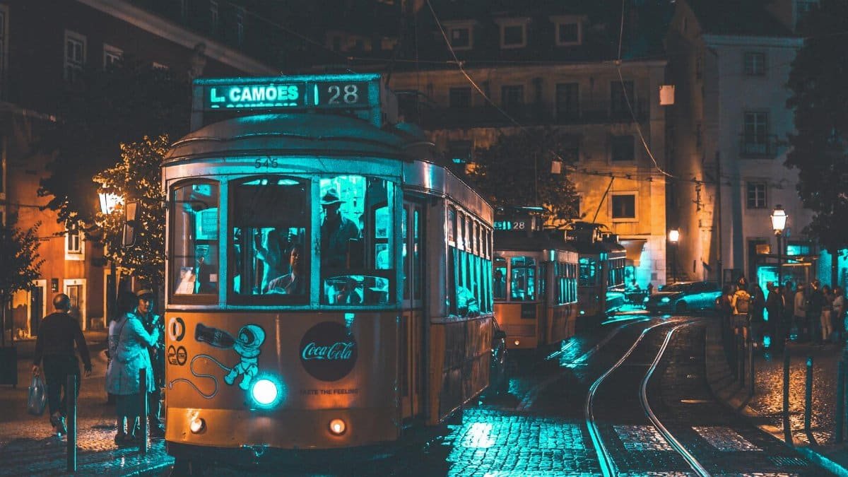Illuminated vintage tram rides through Lisbon at night showcasing urban life and street lighting ambiance.