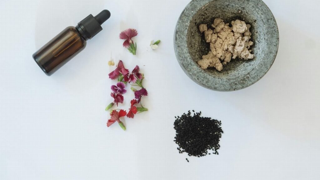 Flat lay of natural skincare ingredients including flowers, black seeds, and a dropper bottle.