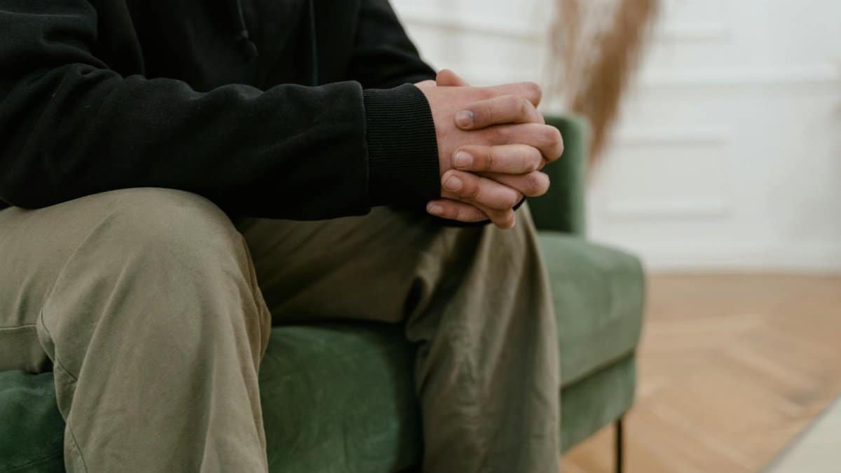Close-up of a person sitting indoors with hands clasped, expressing contemplation.
