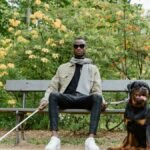 A blind man sits with his guide dog on a park bench, showcasing companionship and support.