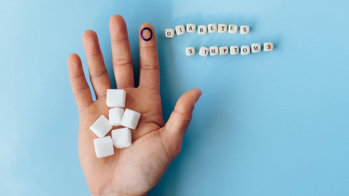 A hand holding sugar cubes with 'Diabetes Symptoms' spelled out, promoting awareness.