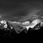 Stunning black and white photo of snow-capped mountains under a dramatic sky.