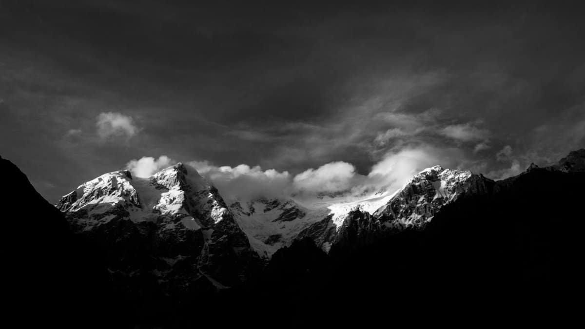Stunning black and white photo of snow-capped mountains under a dramatic sky.