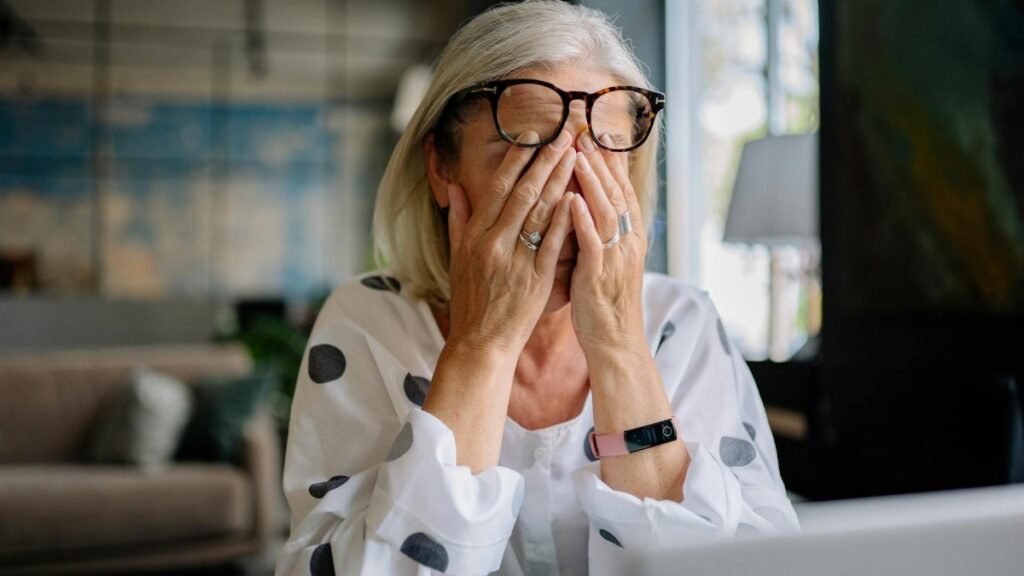 Senior woman experiencing stress indoors, covering face with hands. Reflects emotion and solitude.