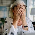 Senior woman experiencing stress indoors, covering face with hands. Reflects emotion and solitude.