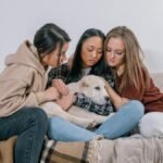 Three women sitting on a couch comforting with a dog, symbolizing support and friendship.