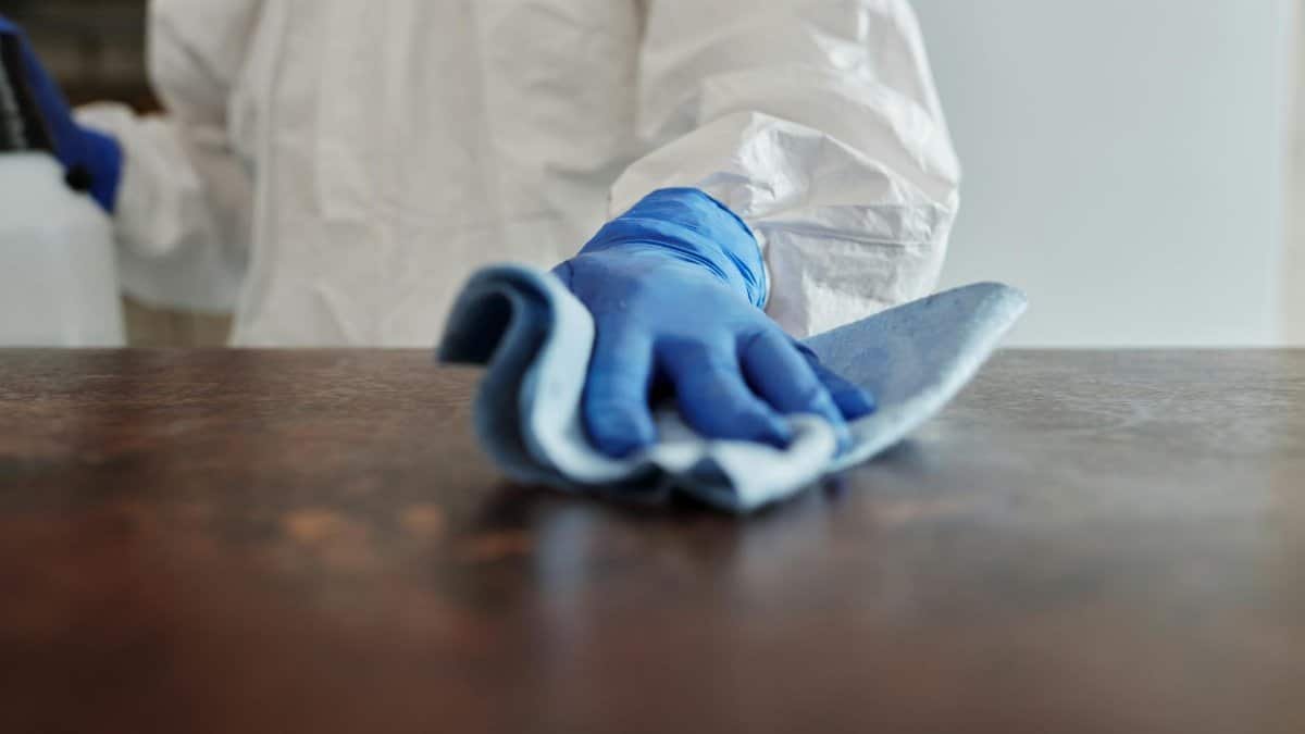 Person in protective suit using disinfectant on surface to ensure cleanliness and safety.
