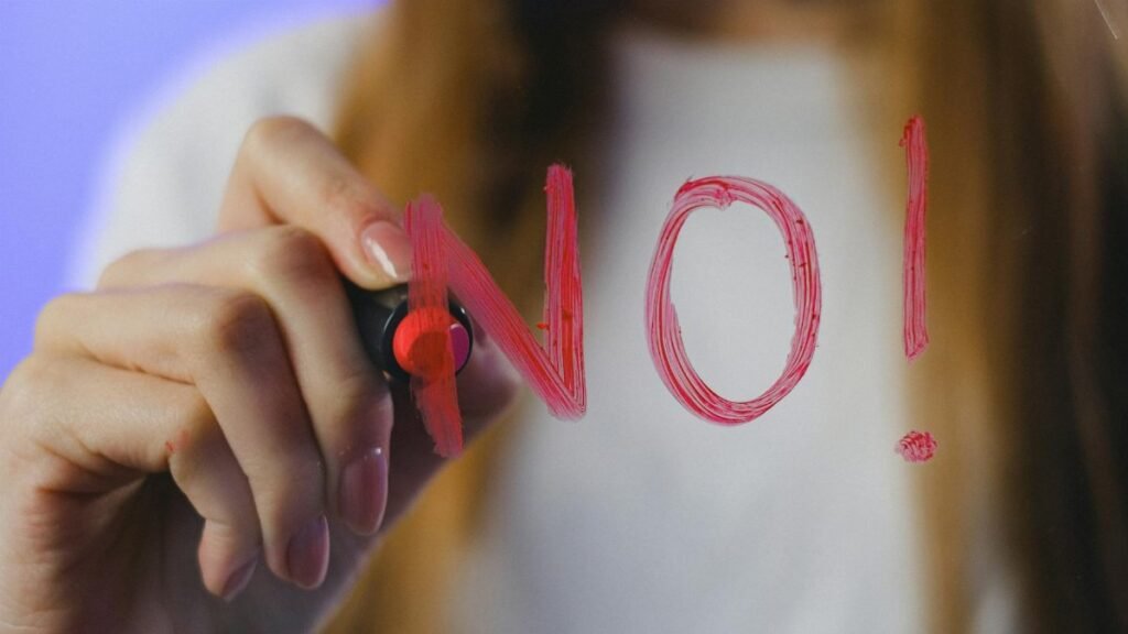 Close-up of teenager writing 'No!' in red on glass, symbolizing refusal, captured in vibrant studio setting.