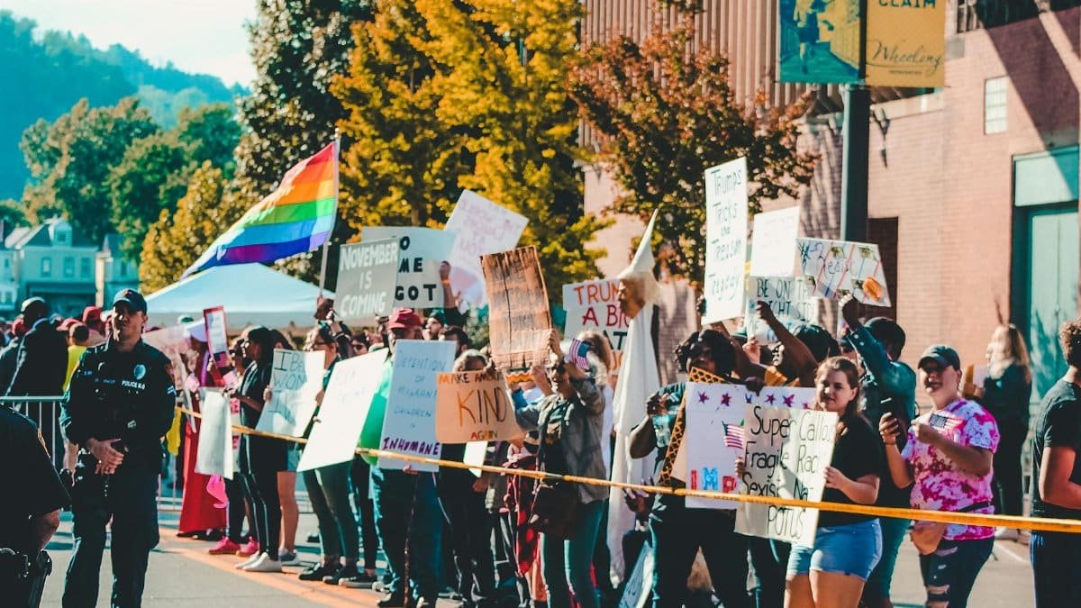 Protesters in Wheeling, WV, hold signs and flags in a diverse, peaceful demonstration on a sunny day.