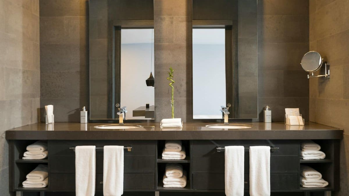 Stylish modern bathroom interior with twin mirrors and towels arranged over sleek dark countertops.