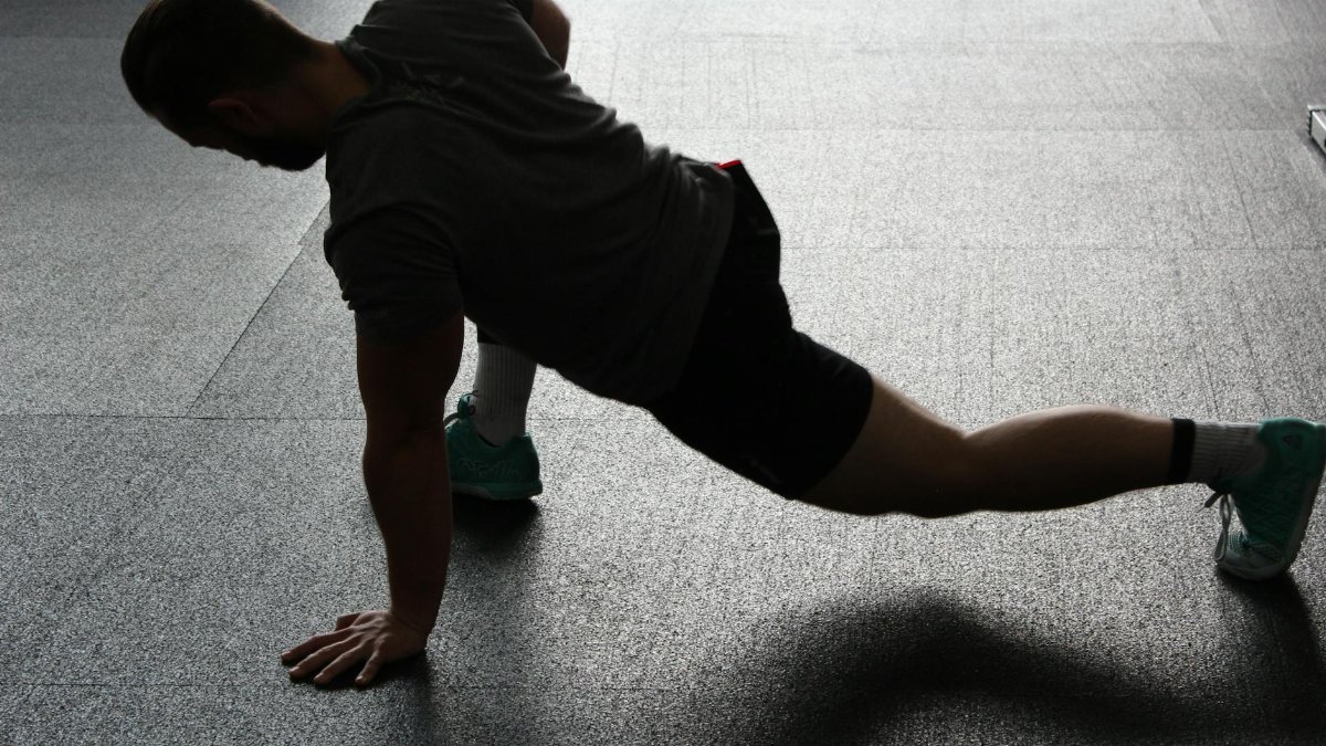 Silhouette of a man executing a stretching routine in a dim gym environment.
