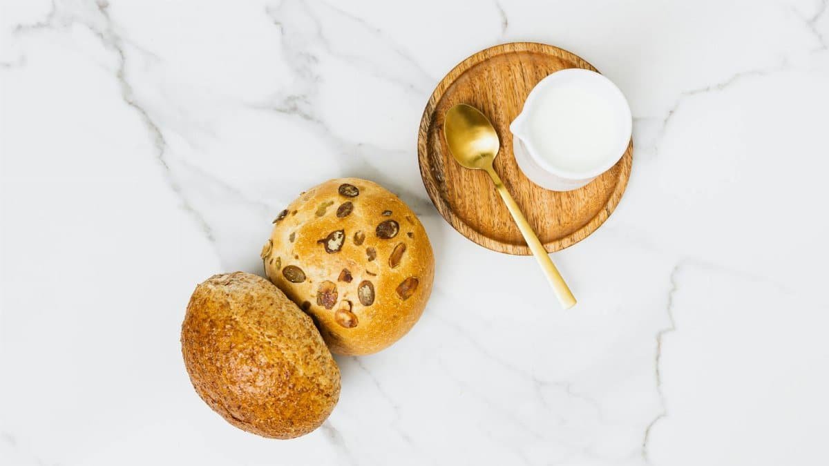 Top view of fresh rolls with milk and a golden spoon on a marble surface.
