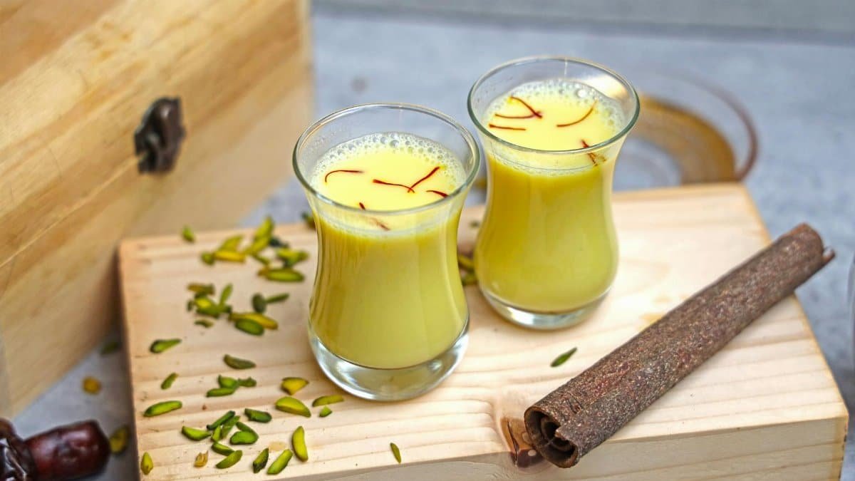 Turmeric and saffron milk on a rustic wooden board, garnished with pistachios.