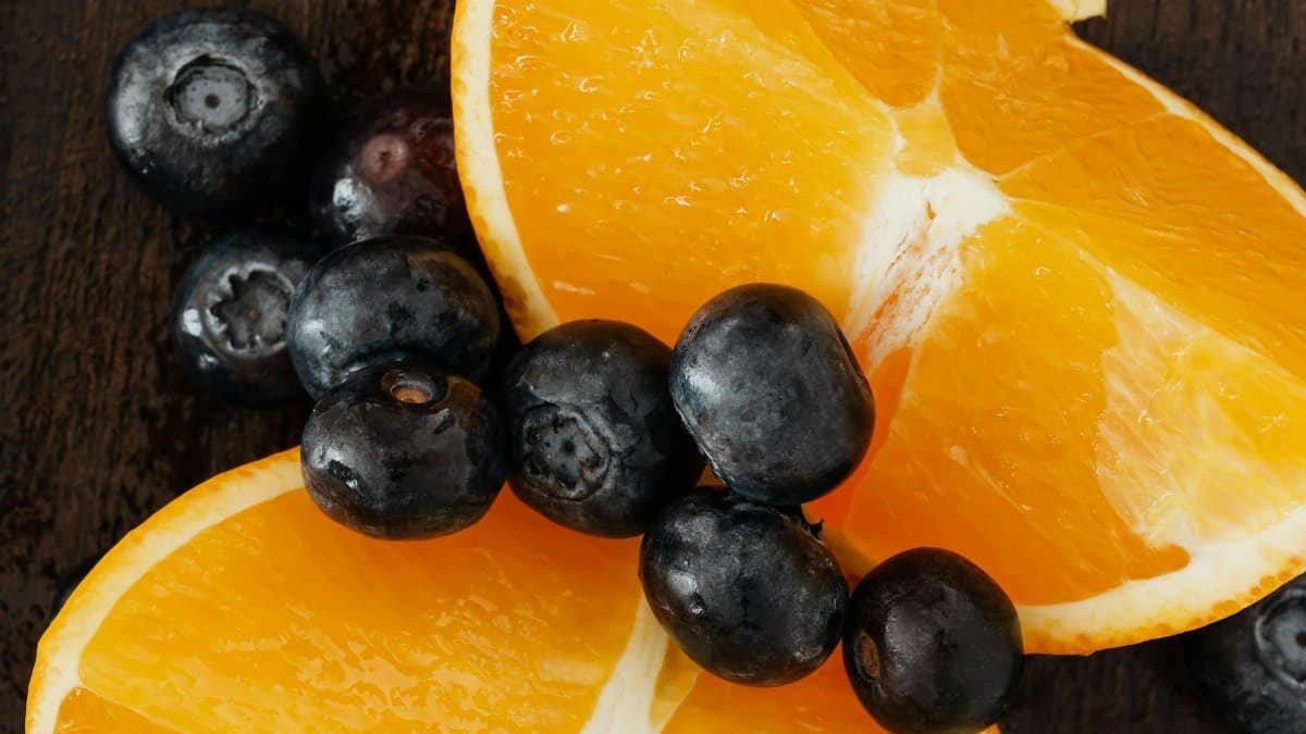 From above organic blueberries scattered on halves of ripe orange on lumber table prepared for raw breakfast