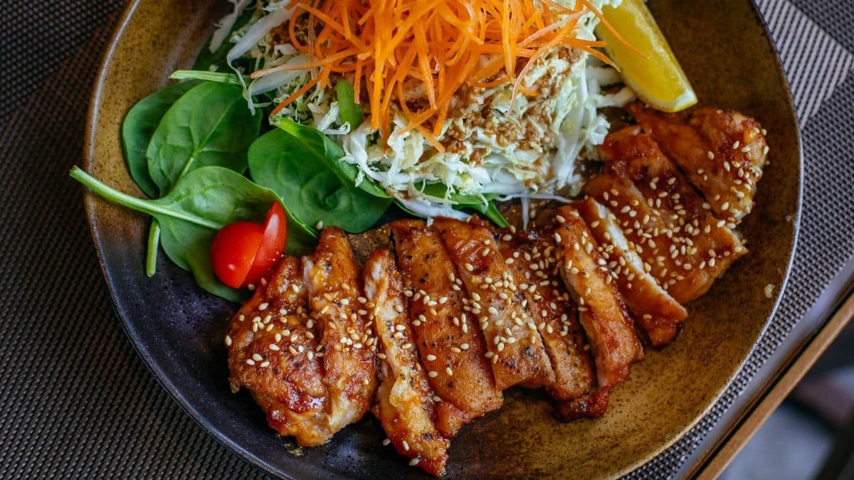 A savory chicken salad bowl garnished with sesame seeds, fresh vegetables, and lemon wedge.