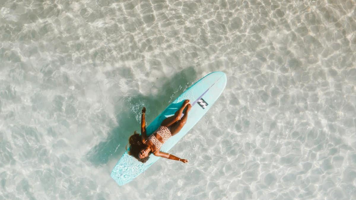 A woman in leopard print swimwear relaxes on a surfboard in clear waters, showcasing leisure and summer vibes.