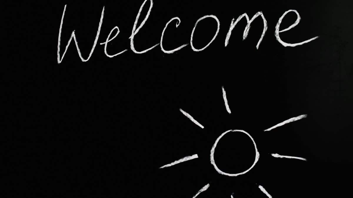 Chalk-drawn 'Welcome' and sun illustration on a black chalkboard background.