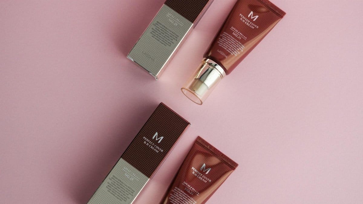 Flat lay of cosmetic products on a pink surface featuring foundation creams.