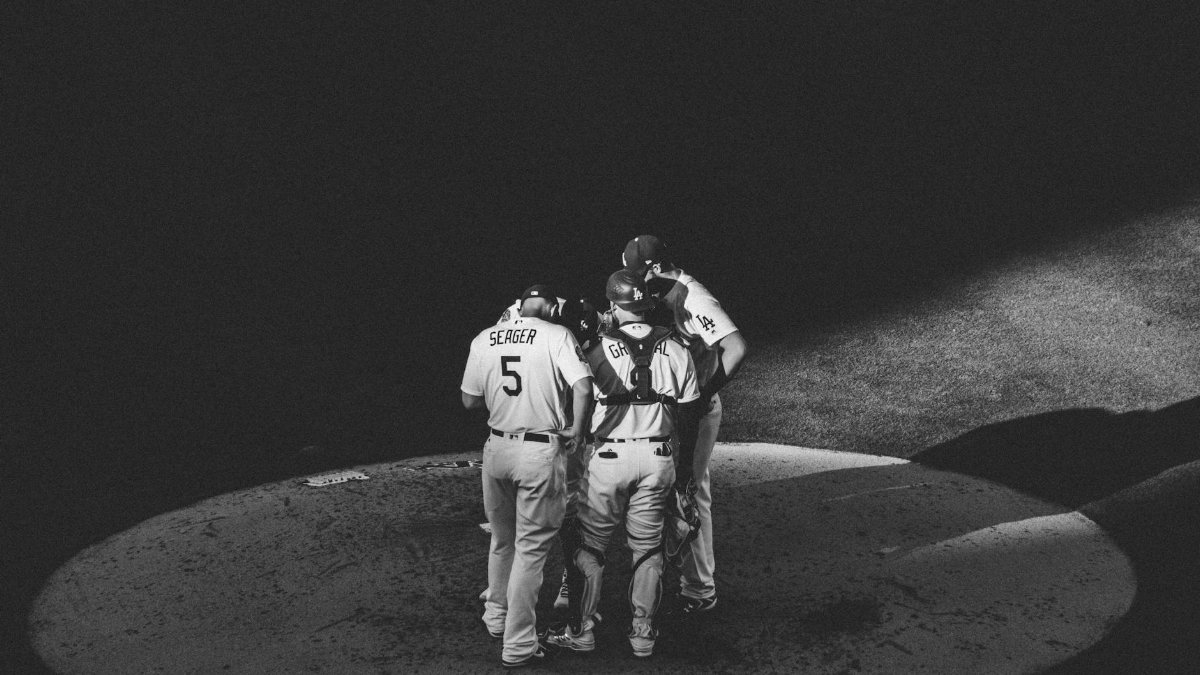 Black and white image of a baseball team huddling on a field under spotlight in Los Angeles, CA.