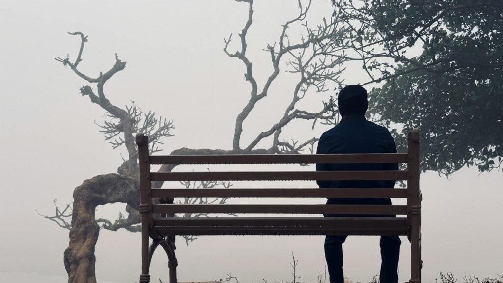 A person sitting alone on a park bench, surrounded by dense fog, creating a serene and introspective mood.