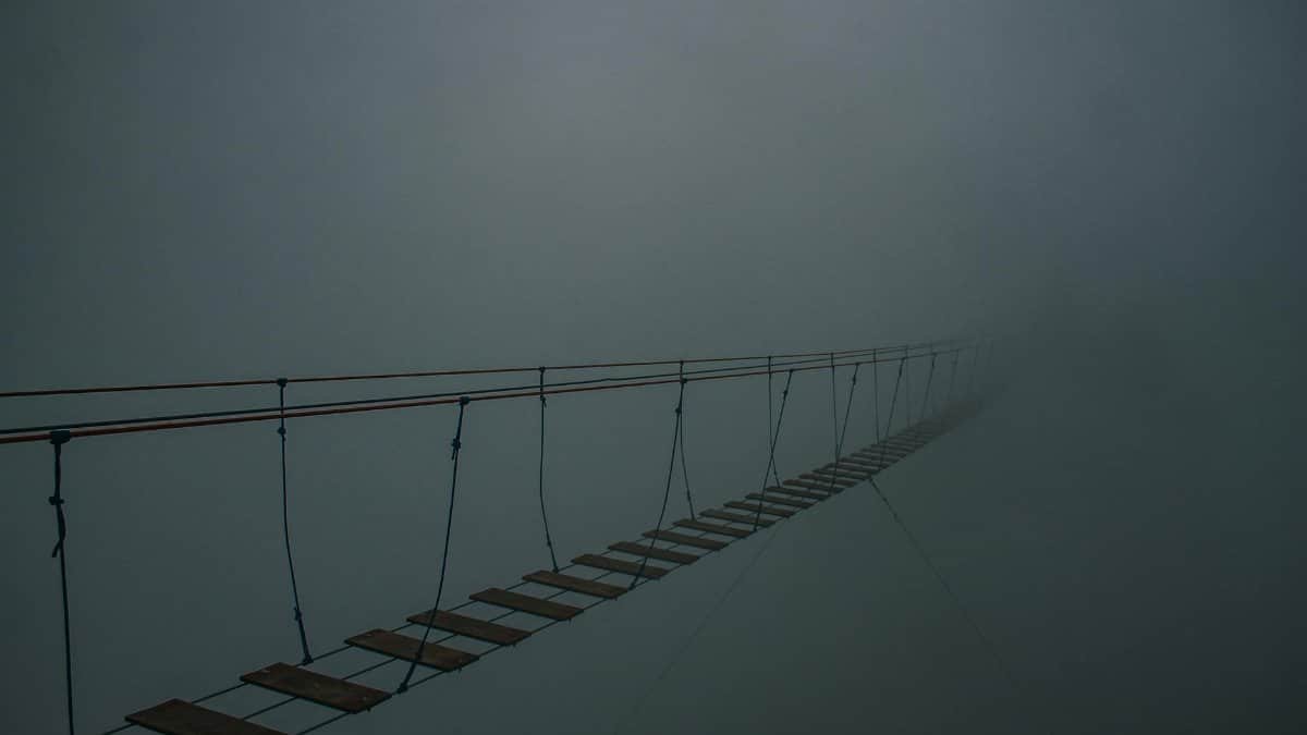 Spooky suspension bridge vanishing into a dense fog, creating a mysterious atmosphere.