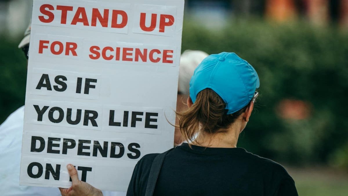 Back view of person holding a protest sign advocating for science in a public setting.