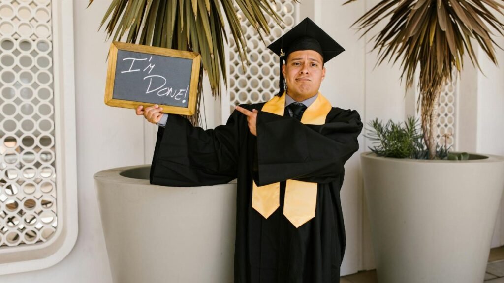 Adult male graduate in cap and gown holding 'I'm Done!' sign outdoors.