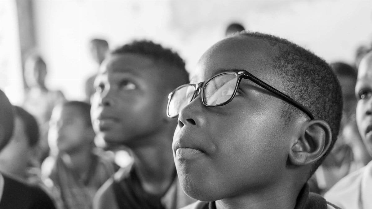 Black and white portrait of attentive children looking upwards in a classroom environment.