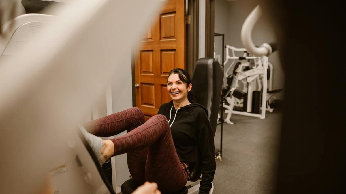 Smiling woman exercising on gym machine indoors, focusing on fitness.