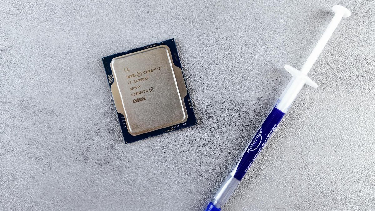 Close-up of an Intel Core i7 processor and syringe of thermal paste on a textured surface.