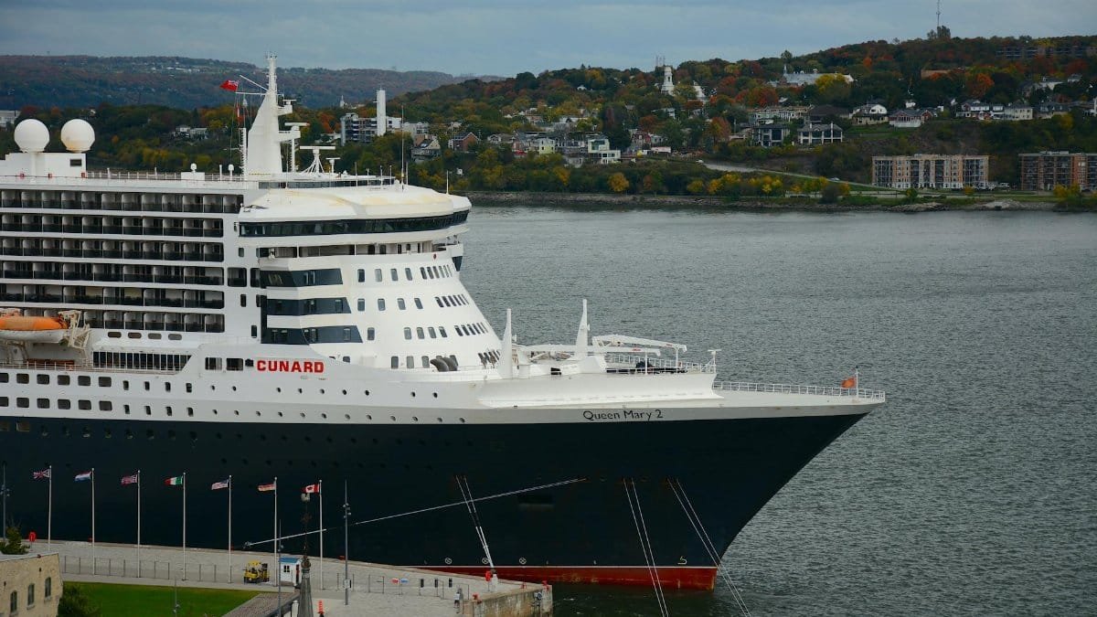 The iconic Queen Mary 2 cruise ship docked at a beautiful harbor with scenic city views.