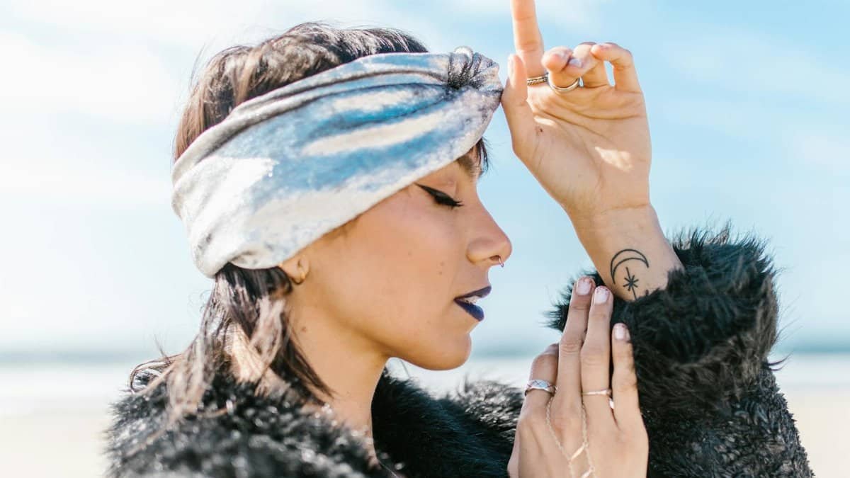 Side profile of a fashionable woman with a celestial tattoo, embracing spirituality by the beach.