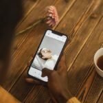 An individual using a dating app on a smartphone with a cup of tea nearby on a wooden table.