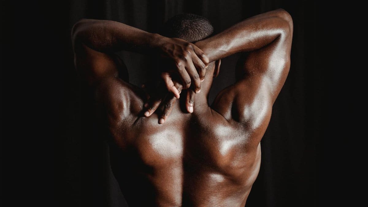 Strong men with defined muscles stretching his back and arms against a dark background.